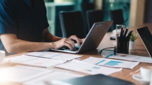 Person working on a laptop with charts and reports, utilizing an association management system for data analysis.